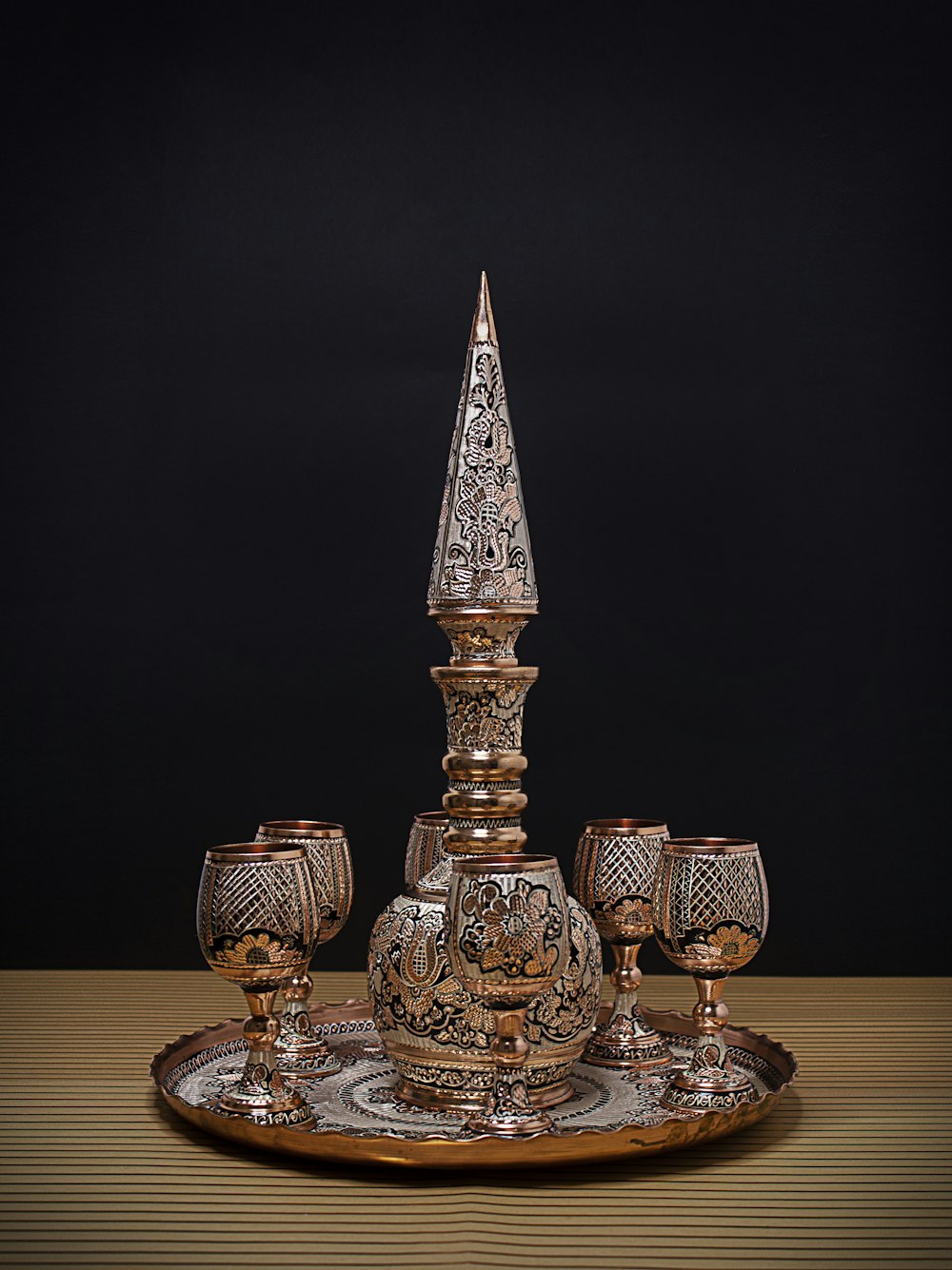 a silver candle holder and four goblets on a wooden table