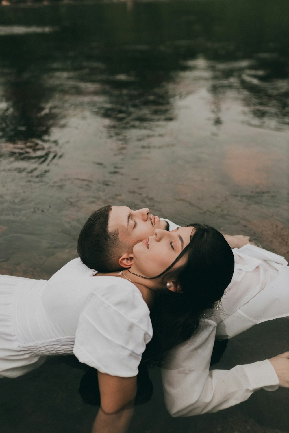 a man and woman laying on the ground next to a body of water