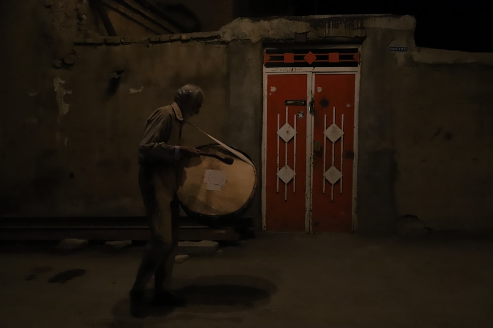 a man holding a large drum in front of a red door