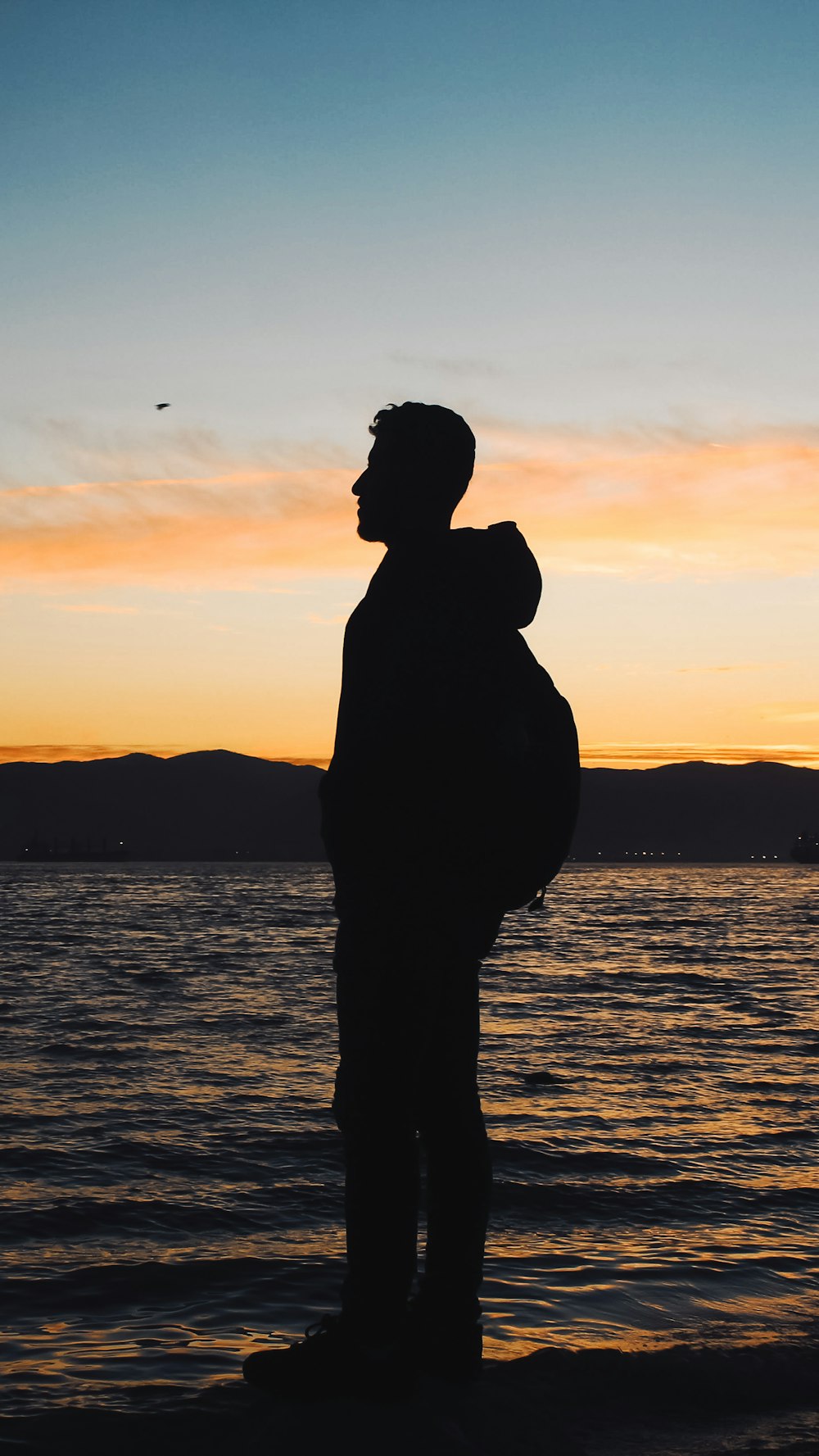 un homme debout sur une plage au coucher du soleil