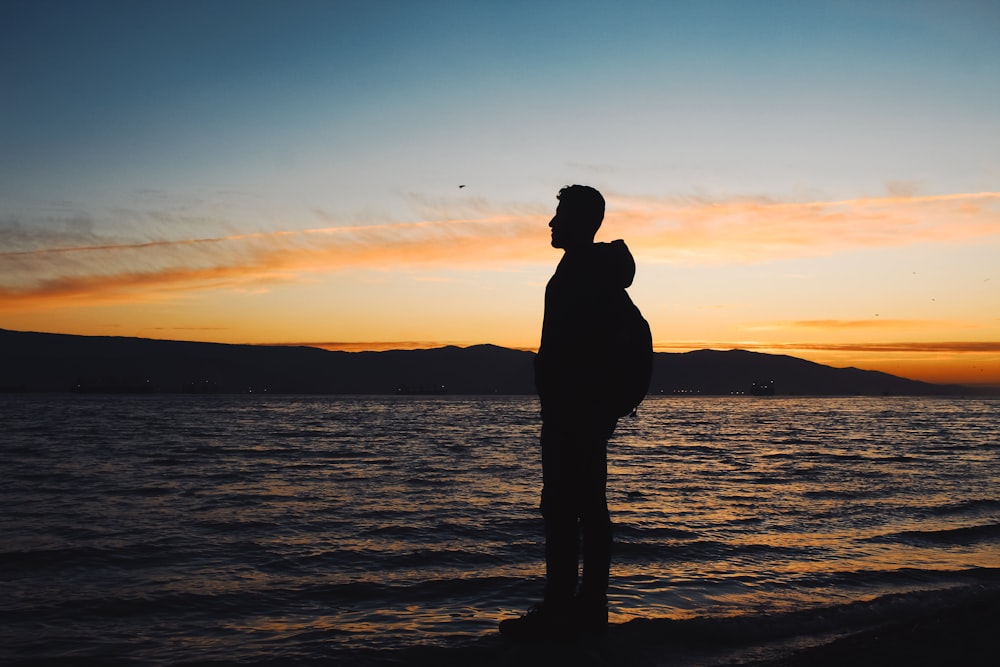 a silhouette of a man standing on a beach at sunset