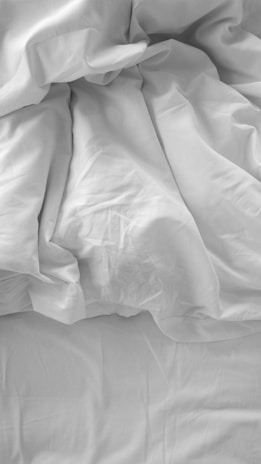 an unmade bed with white sheets and pillows