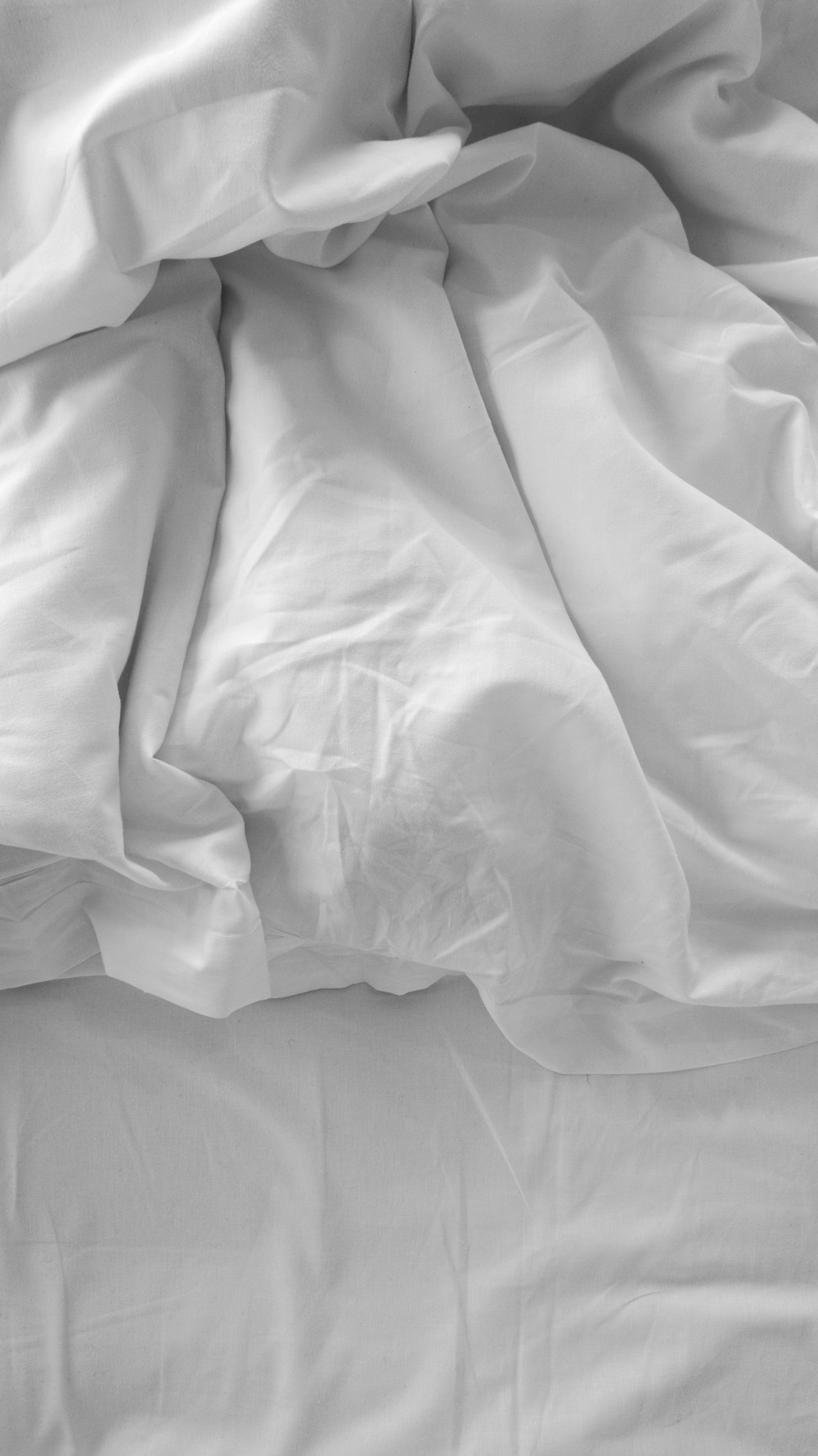 an unmade bed with white sheets and pillows