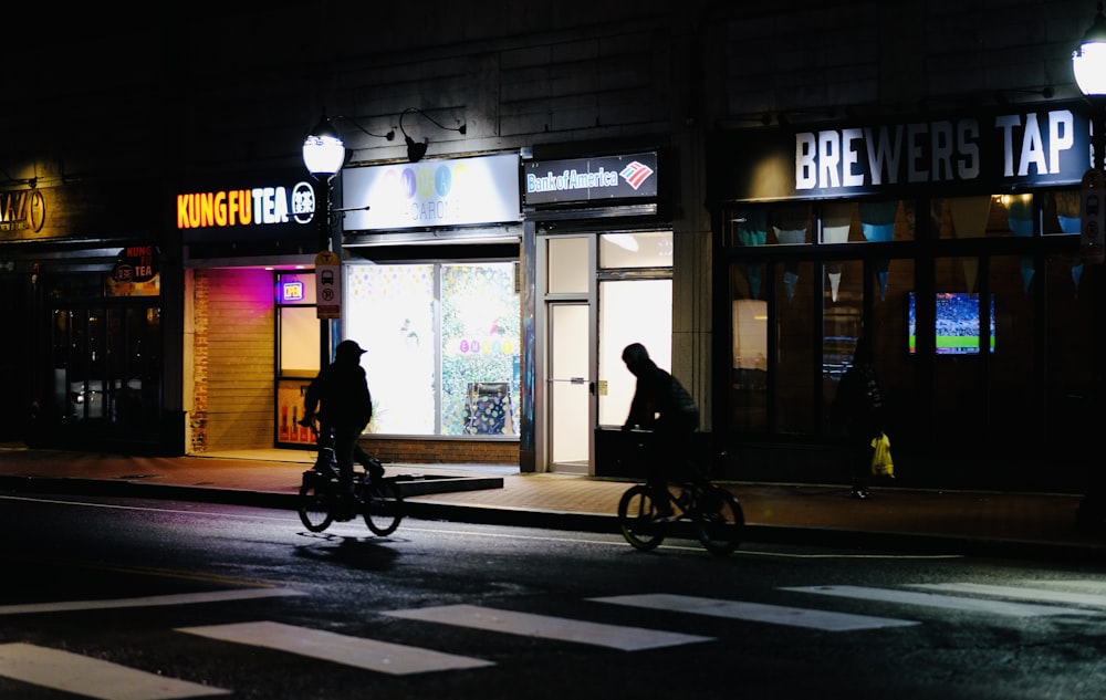 a couple of people riding bikes down a street at night