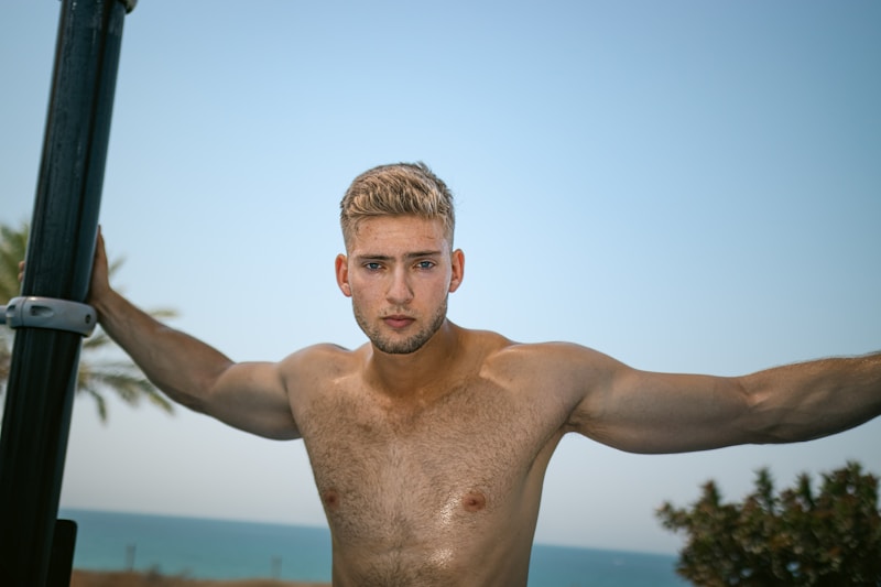 a shirtless man holding a pole by the ocean