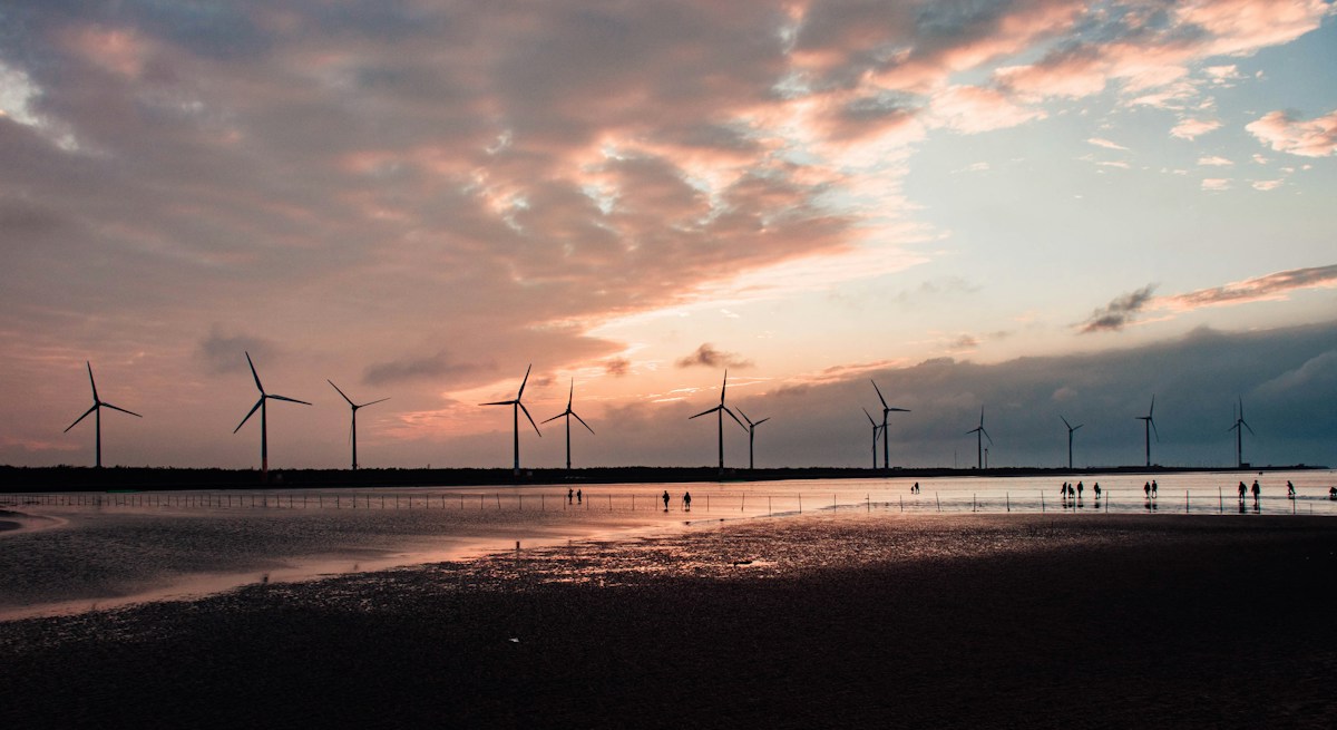Sunset reflections on the mudflats at Gaomei Wetlands with visitors walking in the shallows and wind turbines behind