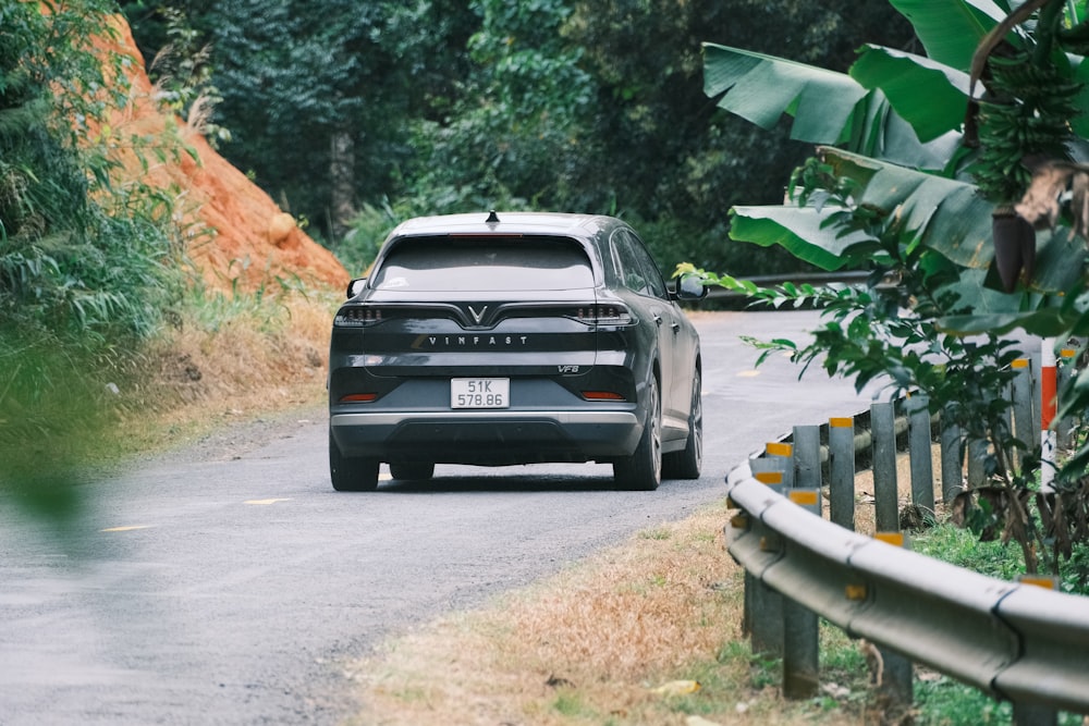 a black car driving down a road next to a lush green forest