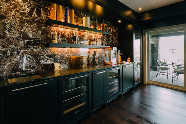Home bar with a dramatic brown and white marble wall, lit shelves and dark cabinets