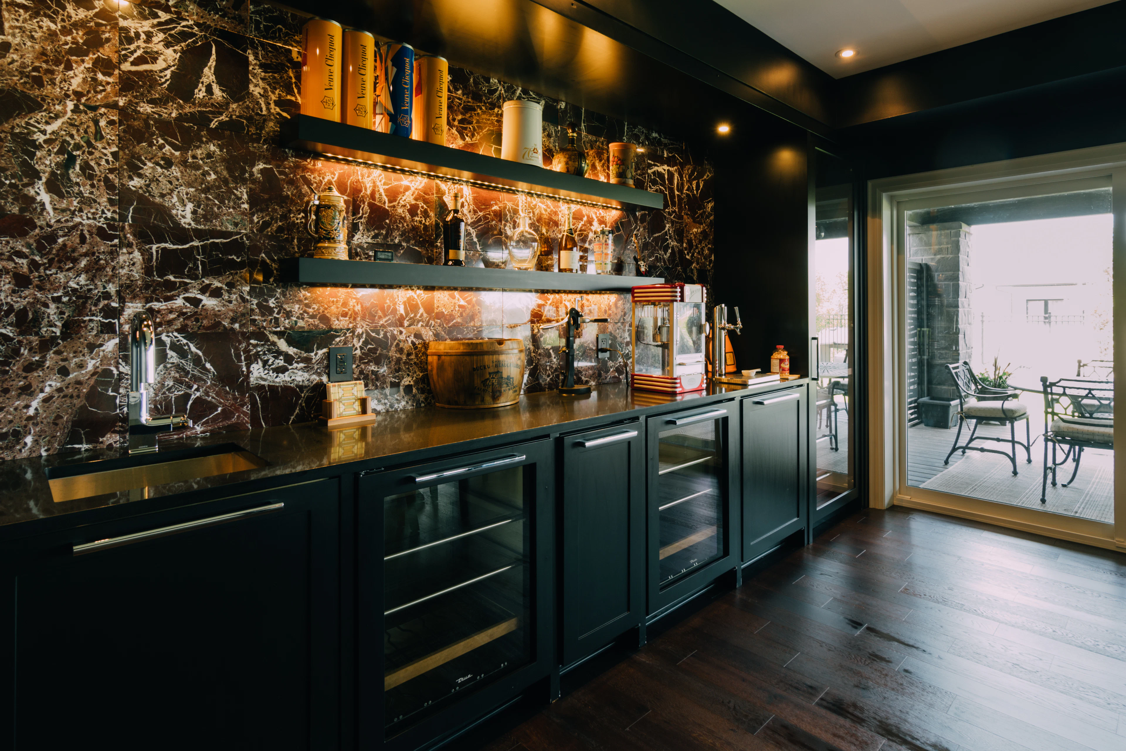 Dark green home bar with stone backsplash and lit shelving