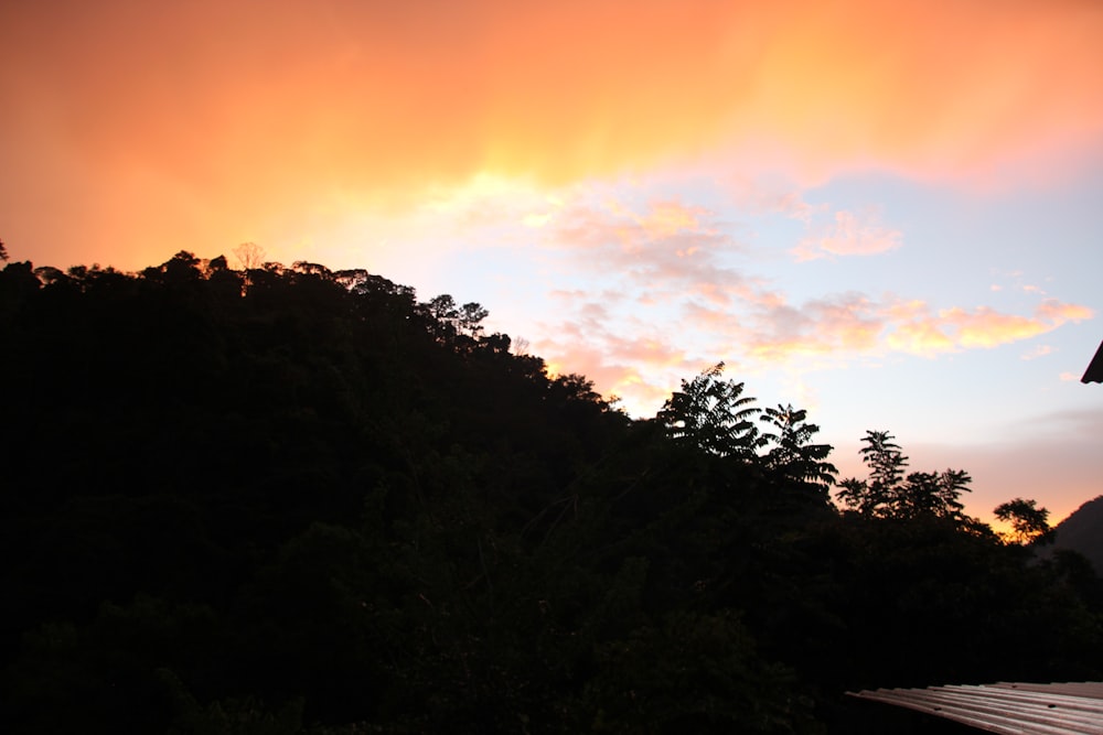 a sunset view of a mountain with clouds and trees