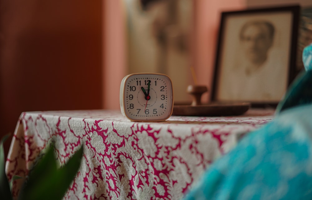 a clock sitting on top of a table next to a potted plant