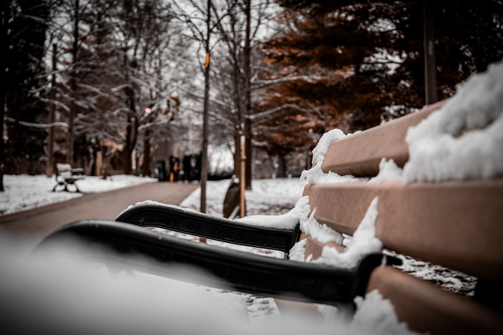 a park bench covered in snow next to a road