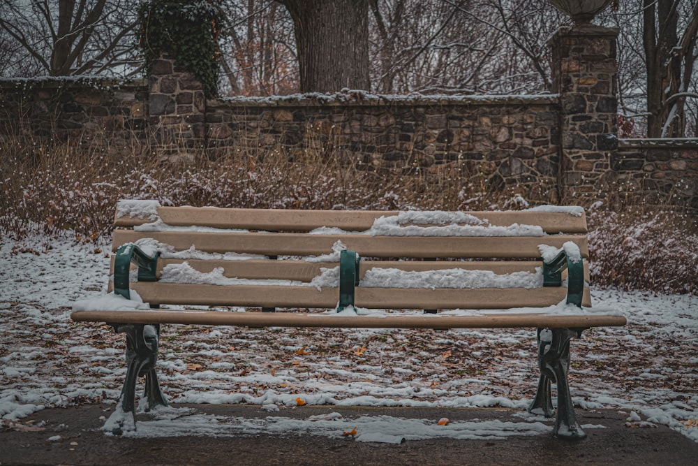 a park bench covered in snow next to a stone wall