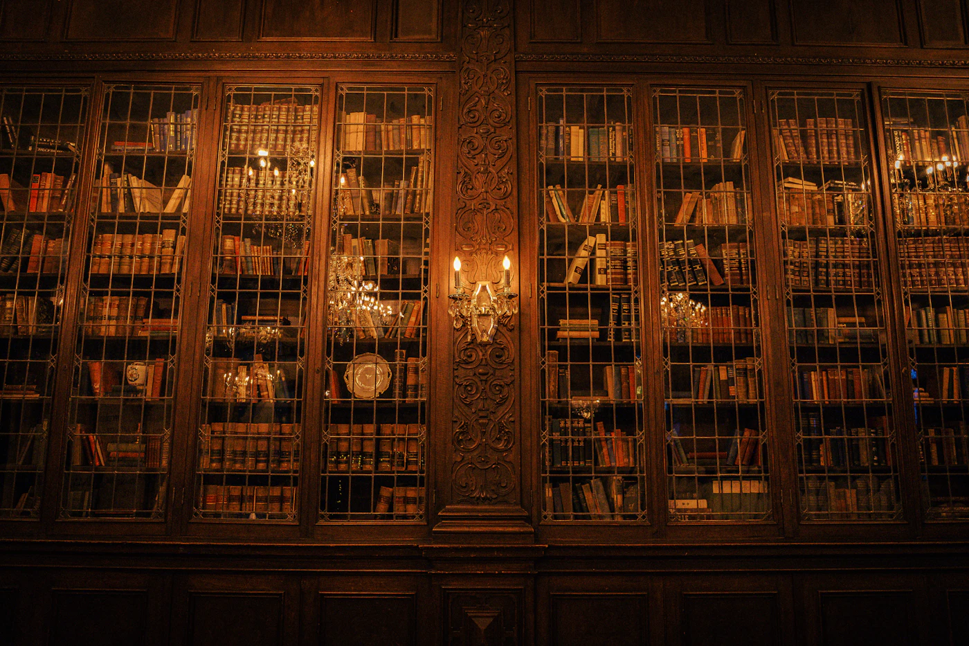 A two-storey library of wooden shelves under warm chandelier light