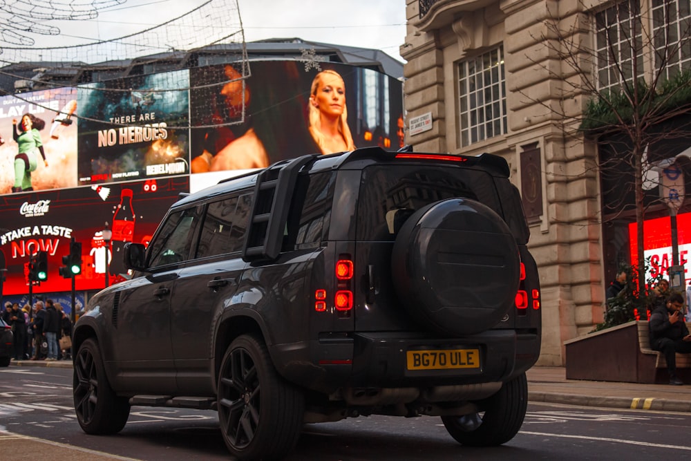 a black suv driving down a street next to tall buildings