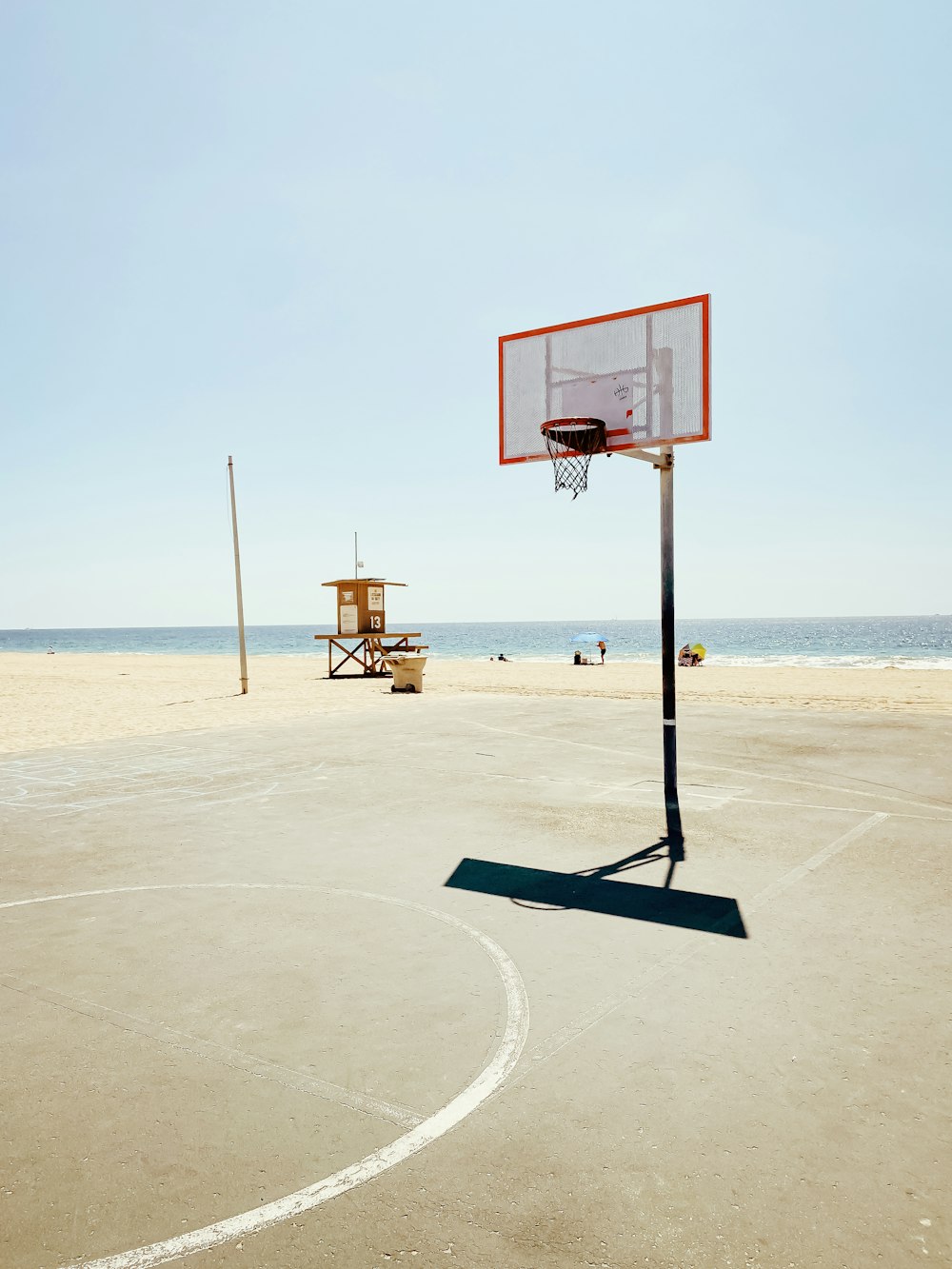 a basketball hoop on the beach with a lifeguard stand in the background