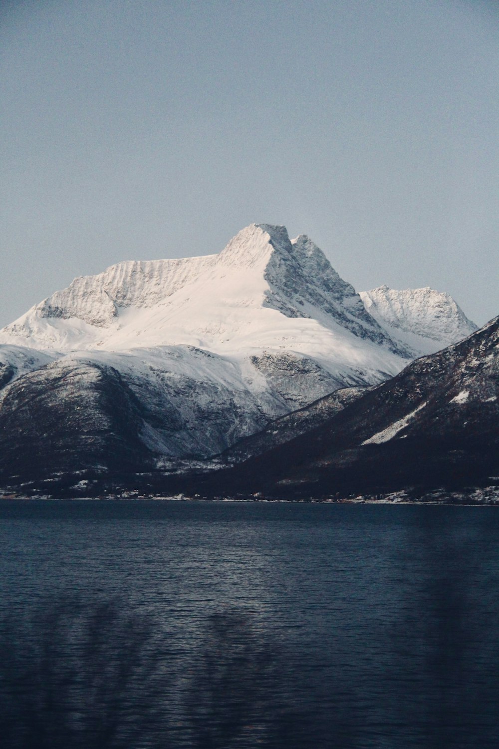 a mountain covered in snow next to a body of water