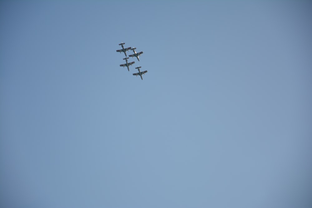 a group of four airplanes flying through a blue sky