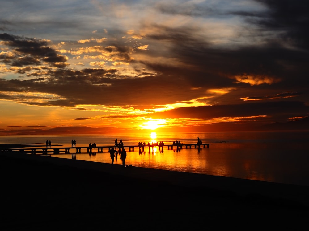 a group of people standing on a pier at sunset