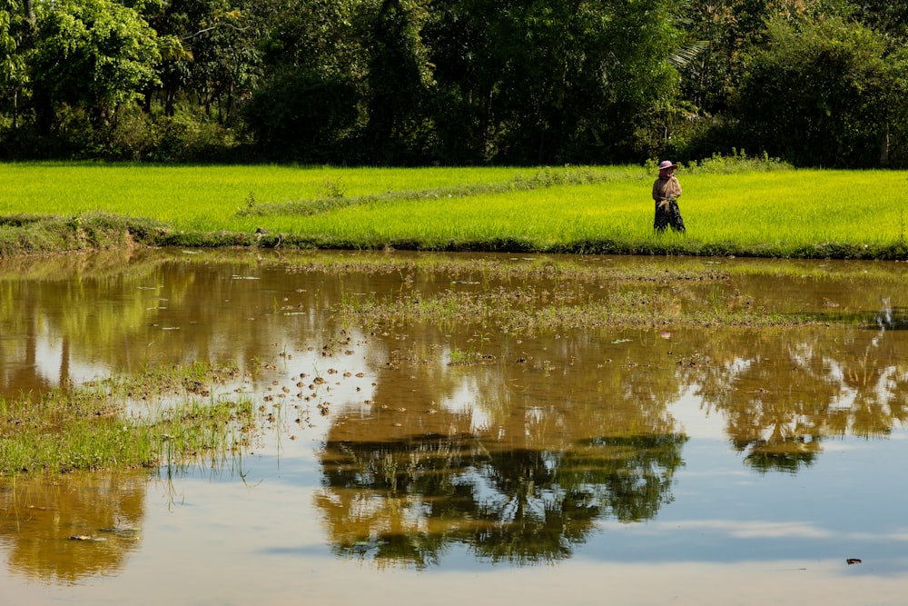 a man standing in a field next to a body of water