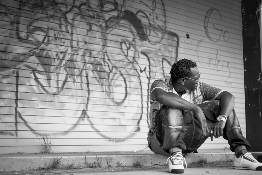 a black and white photo of a man sitting on the curb