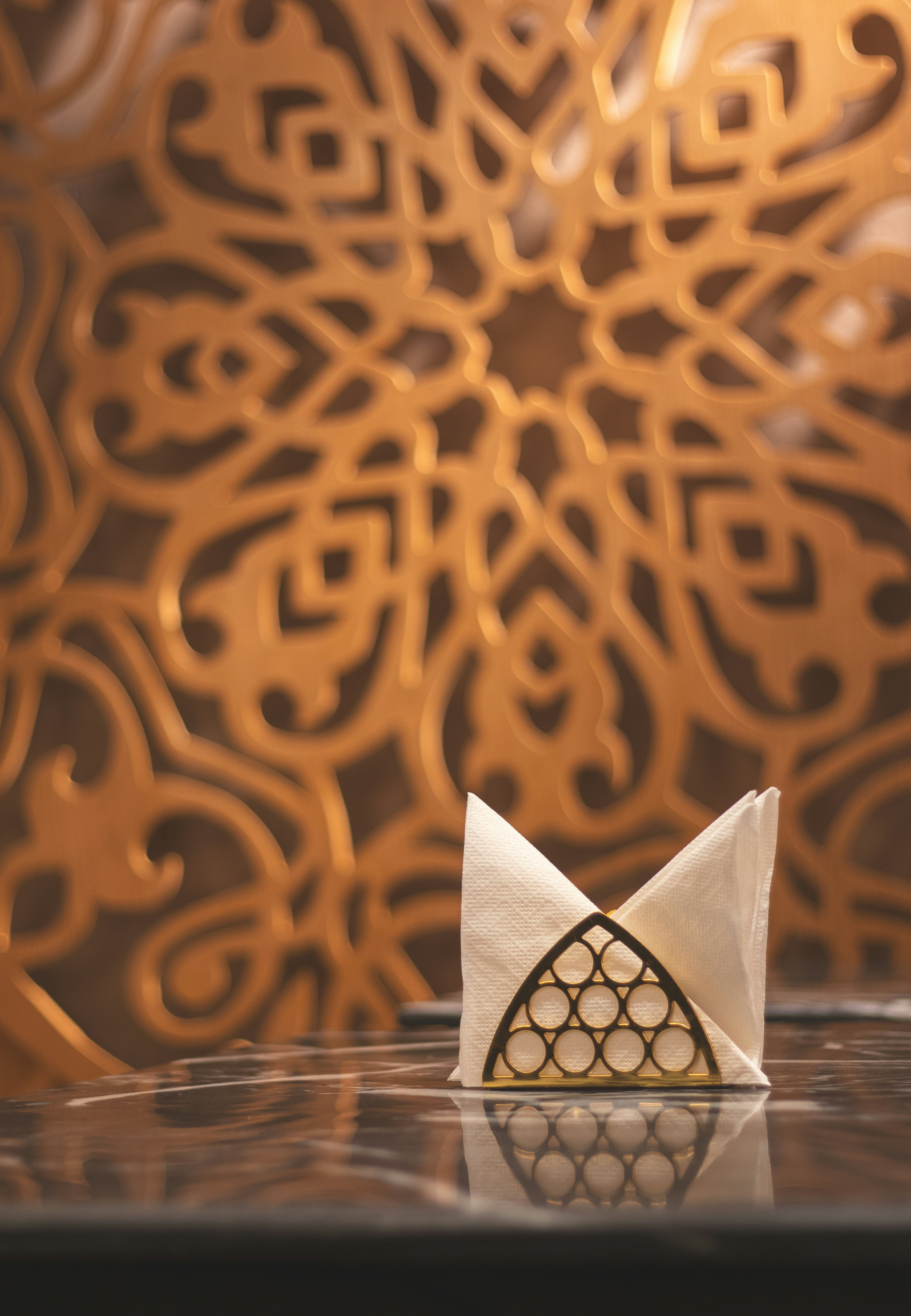 Folded paper napkins sit in a gold patterned metal holder.