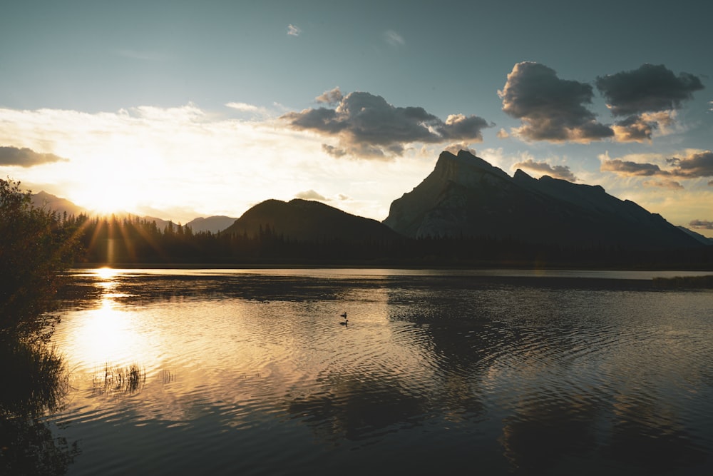 the sun is setting over a lake with mountains in the background