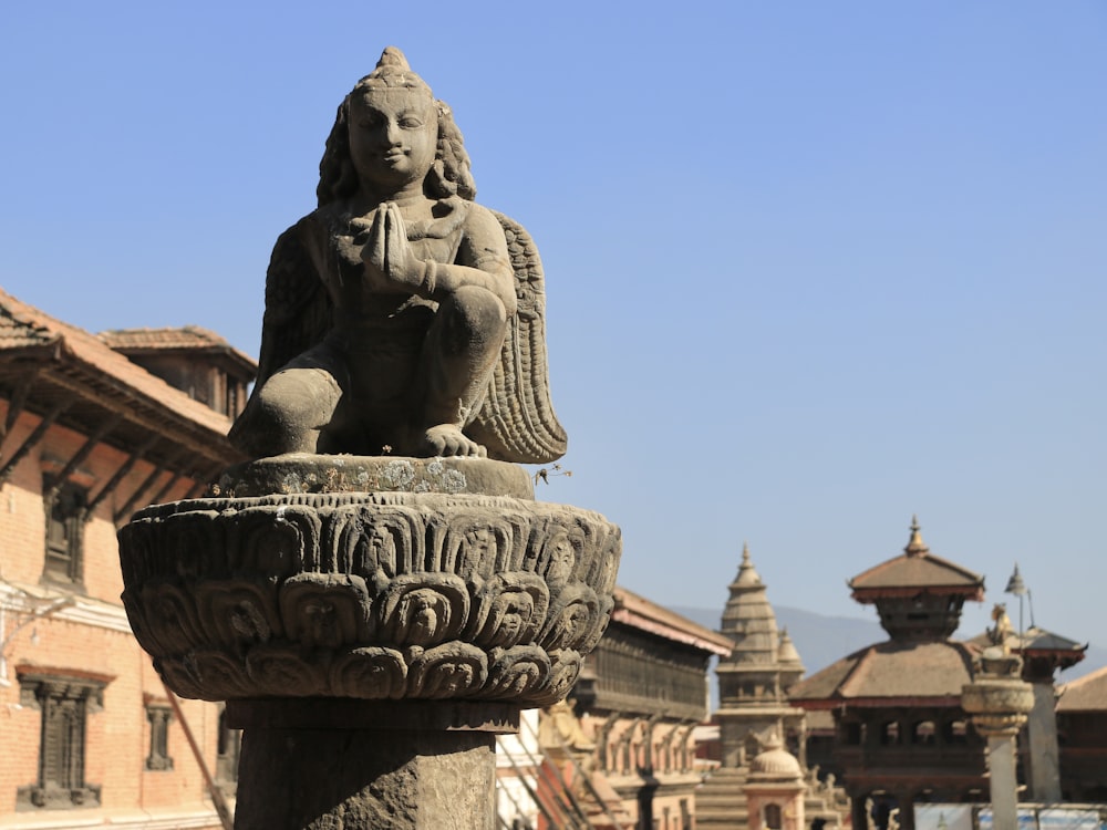 a statue of a person sitting on top of a stone bowl