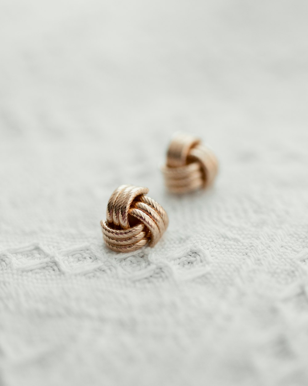 a pair of gold earrings sitting on top of a white cloth