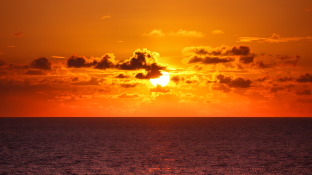 the sun is setting over the ocean on a cloudy day