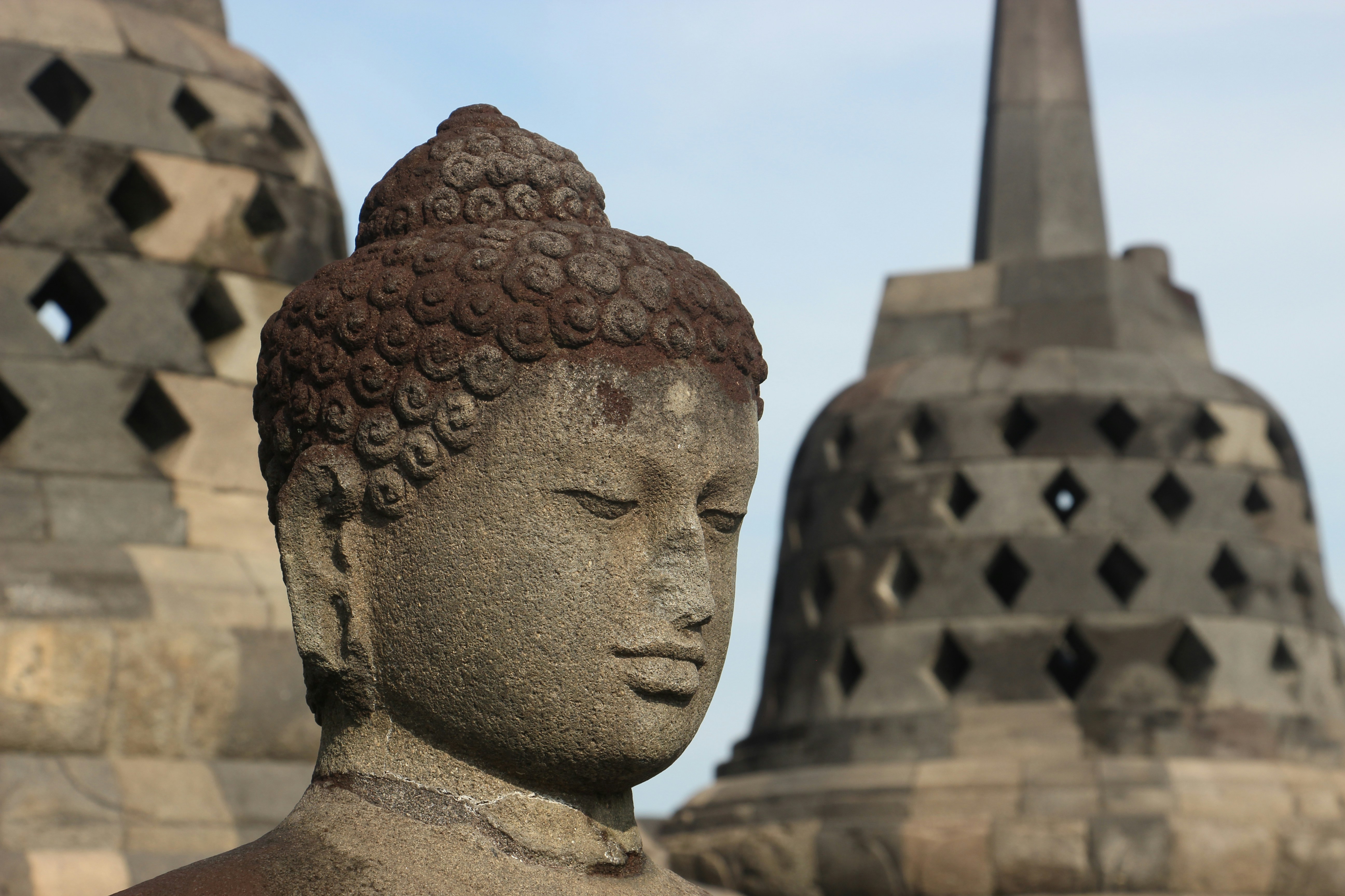 a close up of a statue of a buddha, Capture serenity and history with this evocative photograph featuring the stone-carved countenance of a Buddha statue at Borobudur Temple, Java, Indonesia. The intricate details of the Buddha