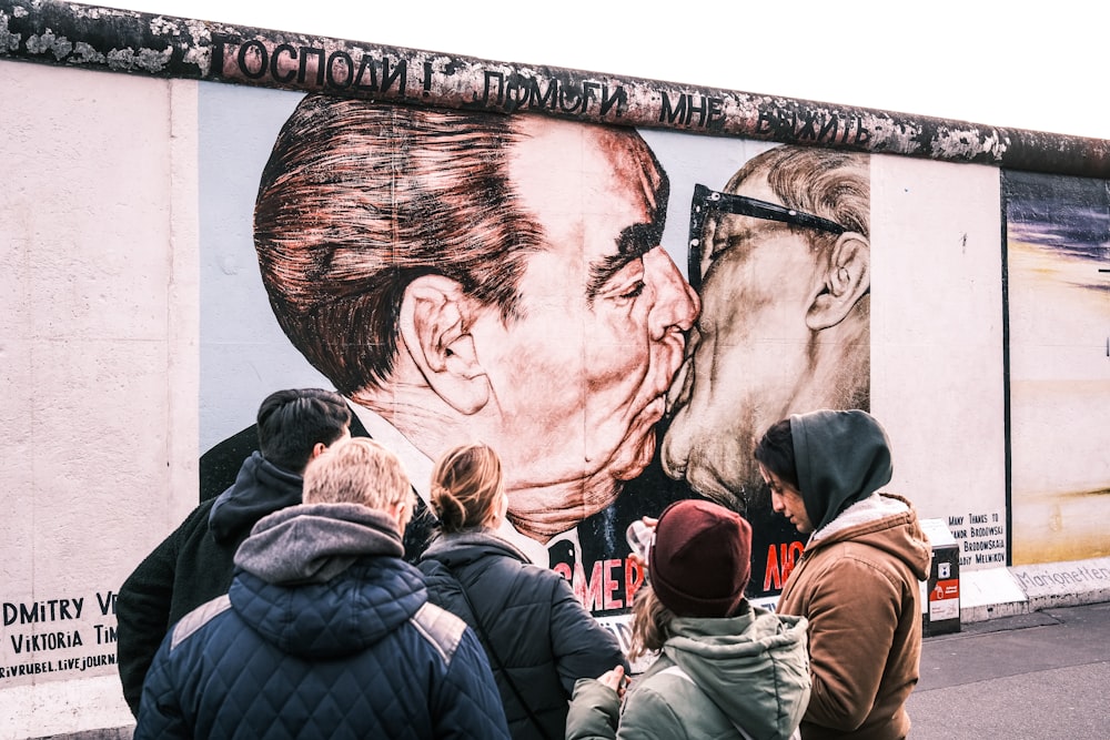 a group of people standing in front of a painting of a man kissing a woman
