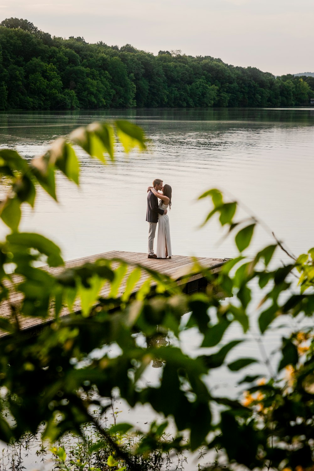 a bride and groom standing on a dock in front of a lake