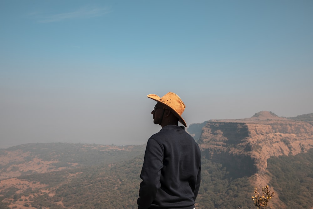 a man wearing a hat standing on top of a mountain