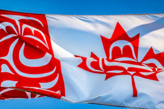 a canadian flag flying in the wind with a blue sky in the background