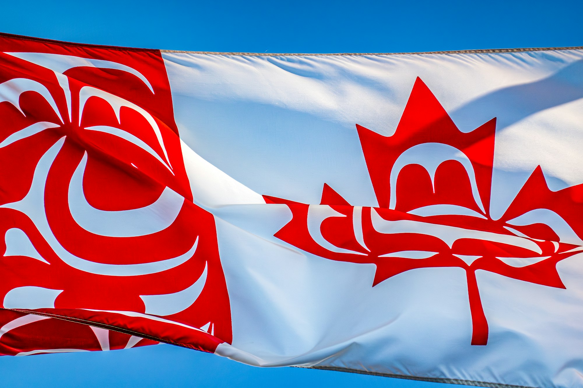 a canadian flag flying in the wind with a blue sky in the background