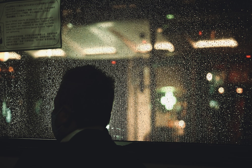 a man looking out a window at a city at night