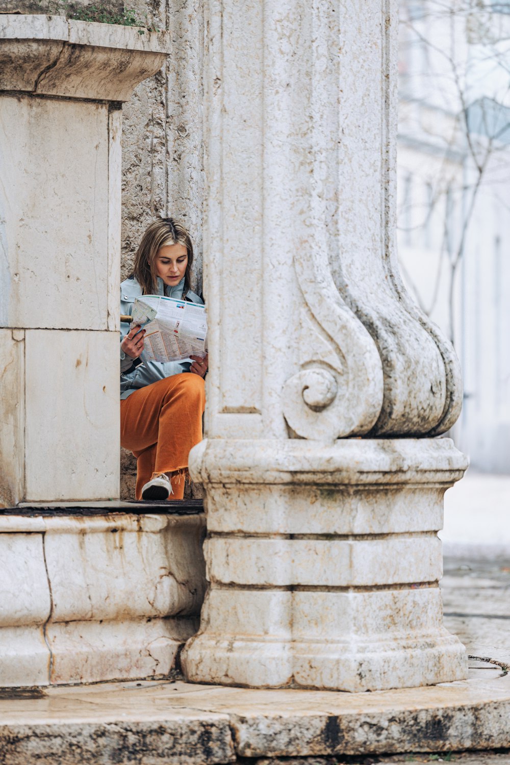 a little girl sitting on a ledge reading a newspaper