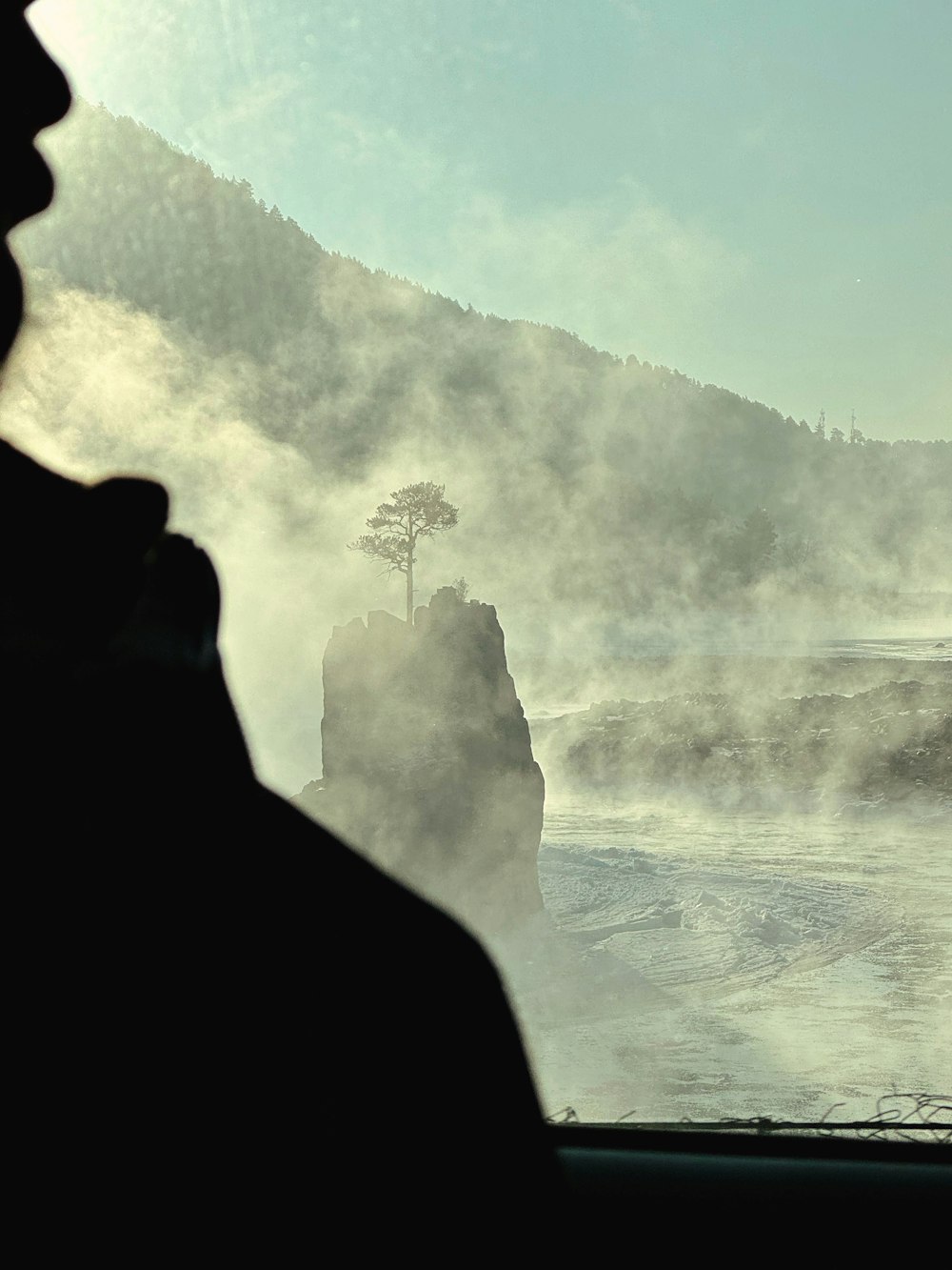 a person looking out a window at a mountain