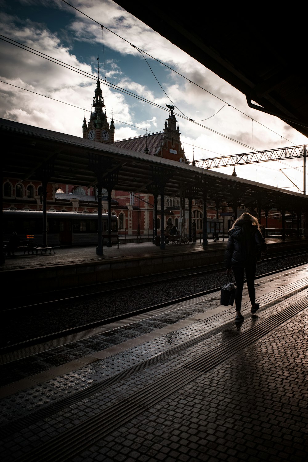a woman walking down a train track next to a train station