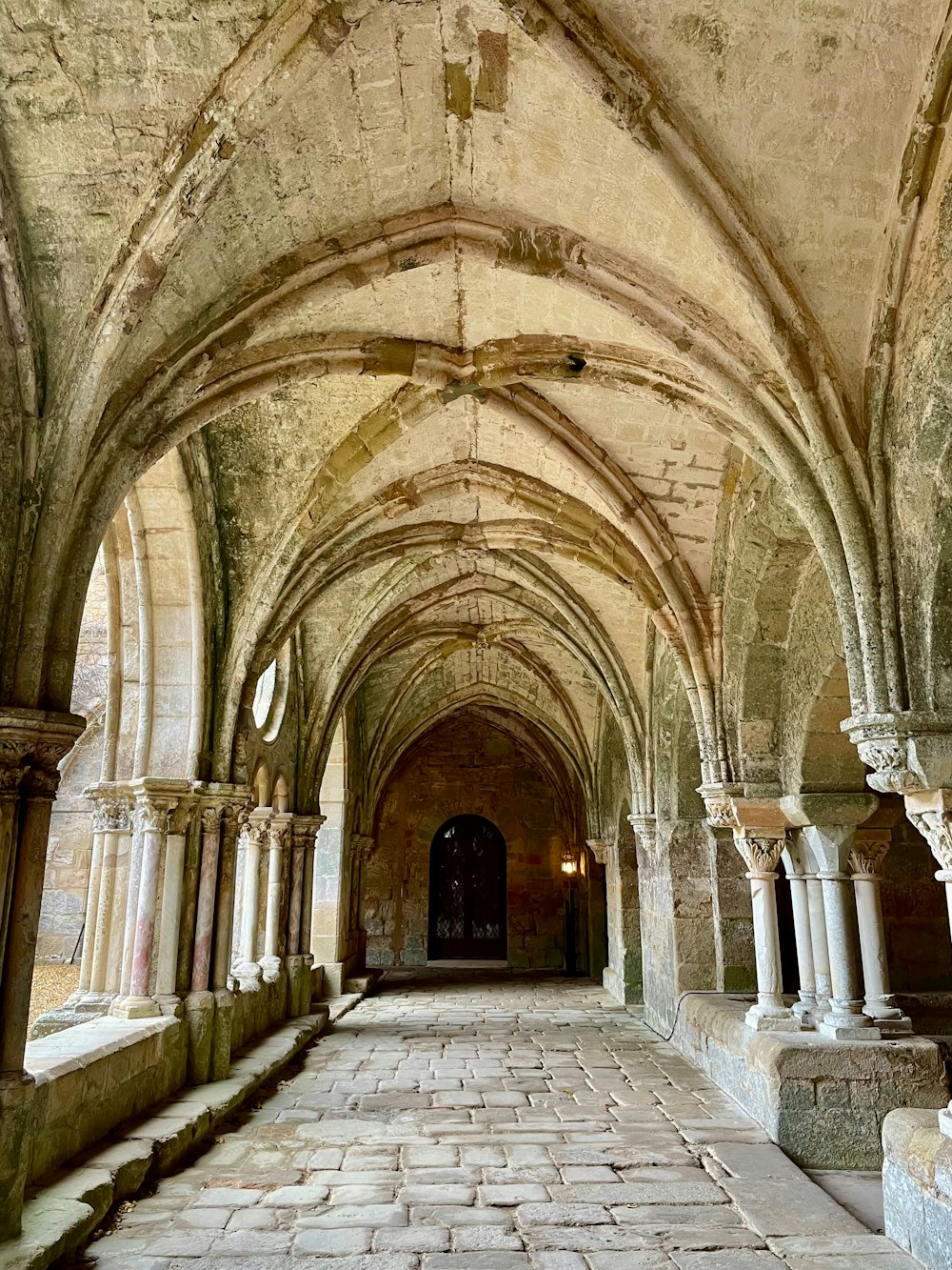 um longo corredor com arcos e piso de pedra