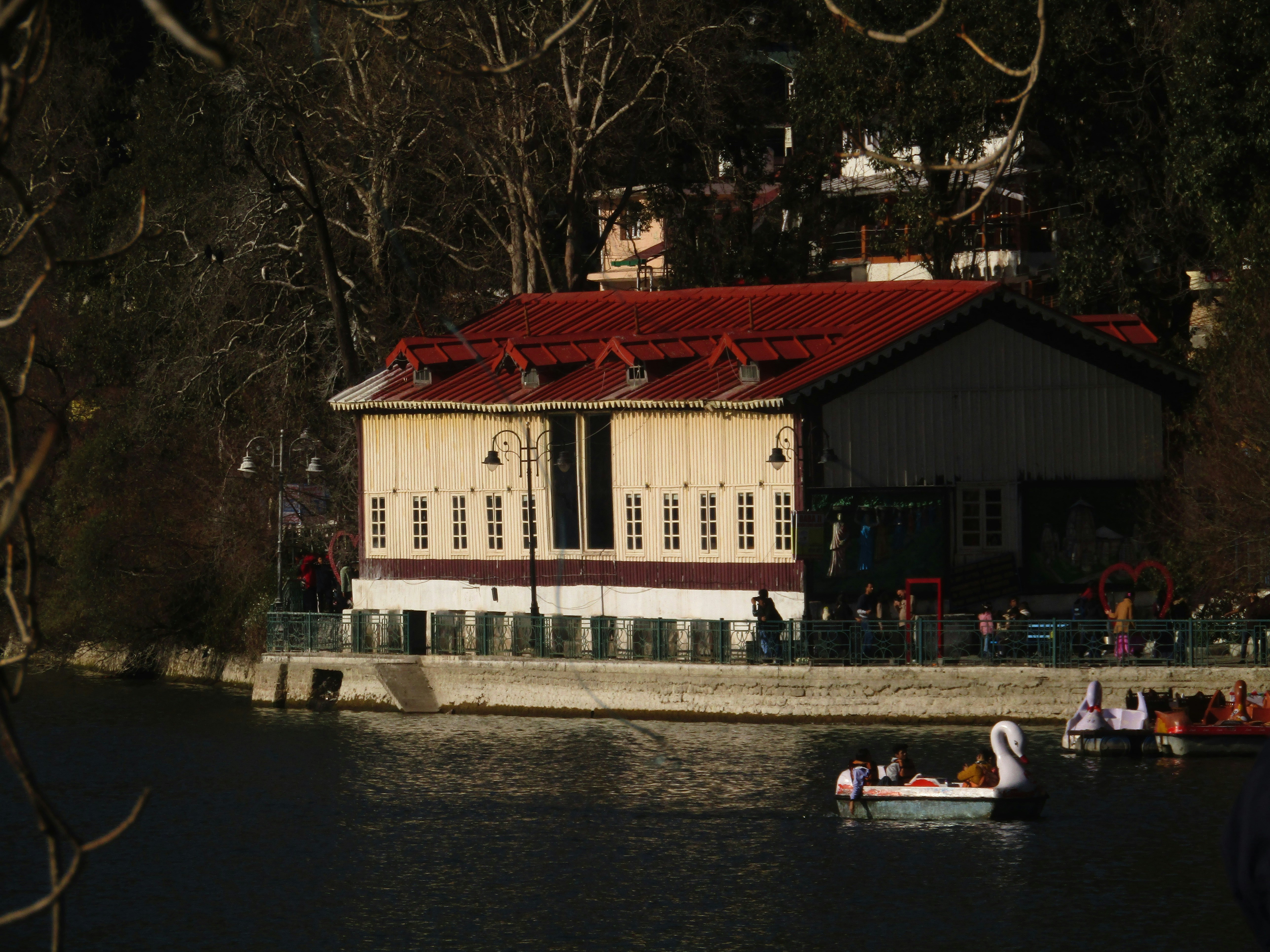 a small boat floating on top of a river next to a building, Building in Nainital lakeside Uttarakhand India