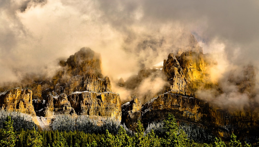 a mountain covered in clouds and trees under a cloudy sky