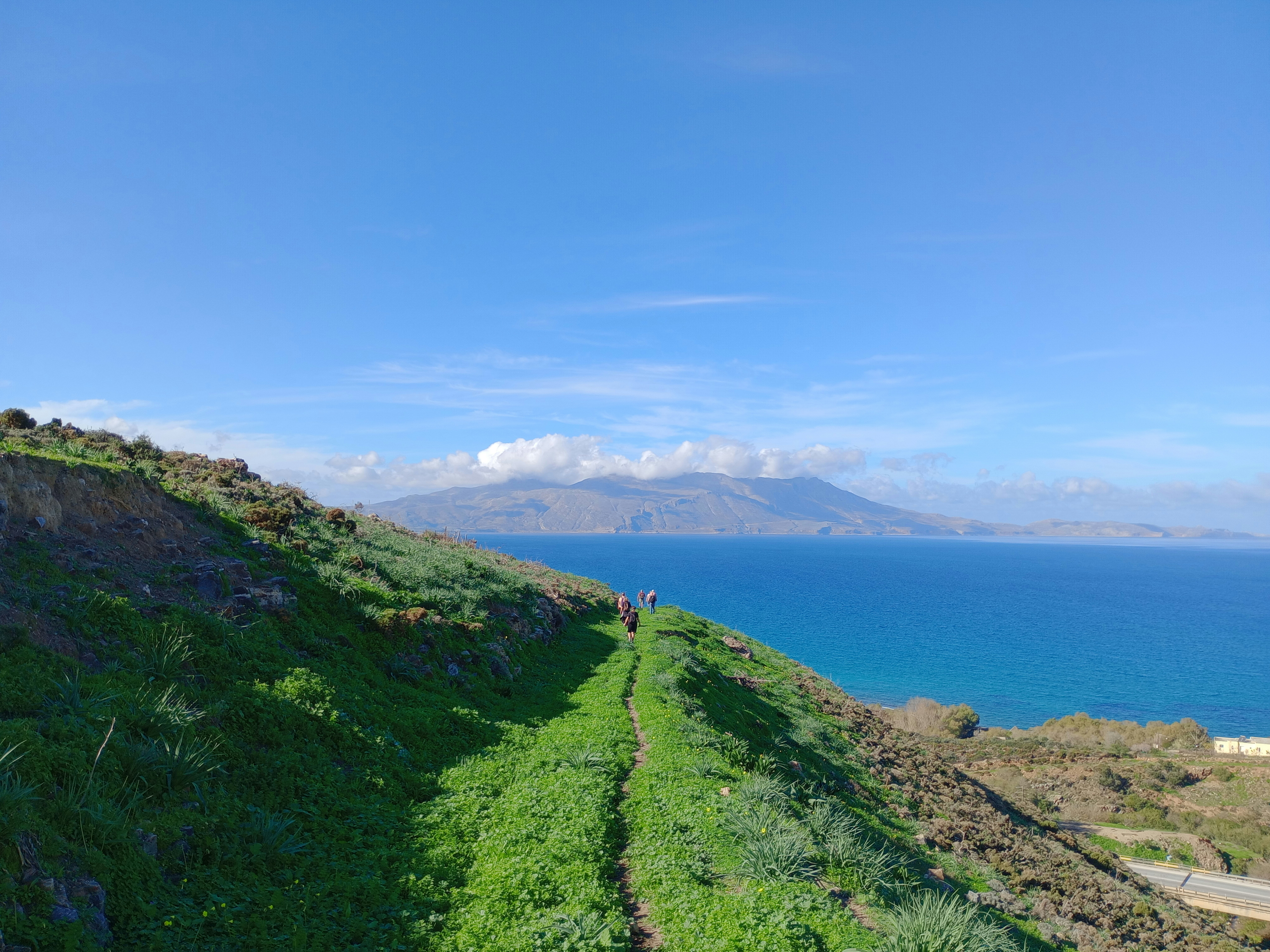 a group of people walking up a hill next to the ocean, 