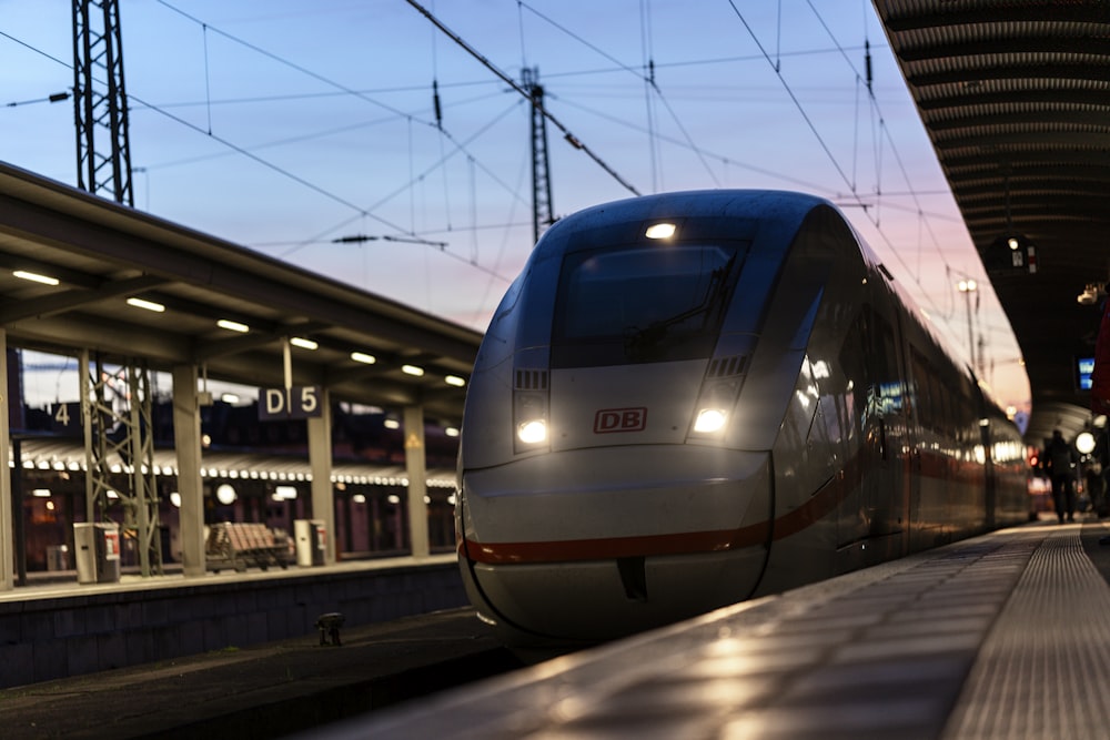 a silver train traveling down train tracks next to a train station