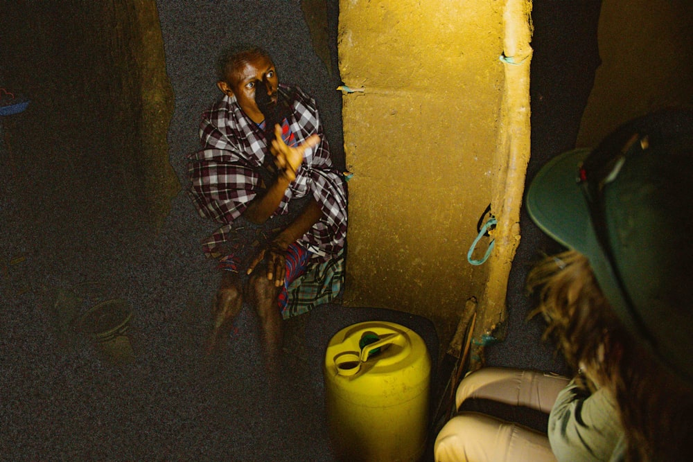 a man sitting next to a yellow trash can