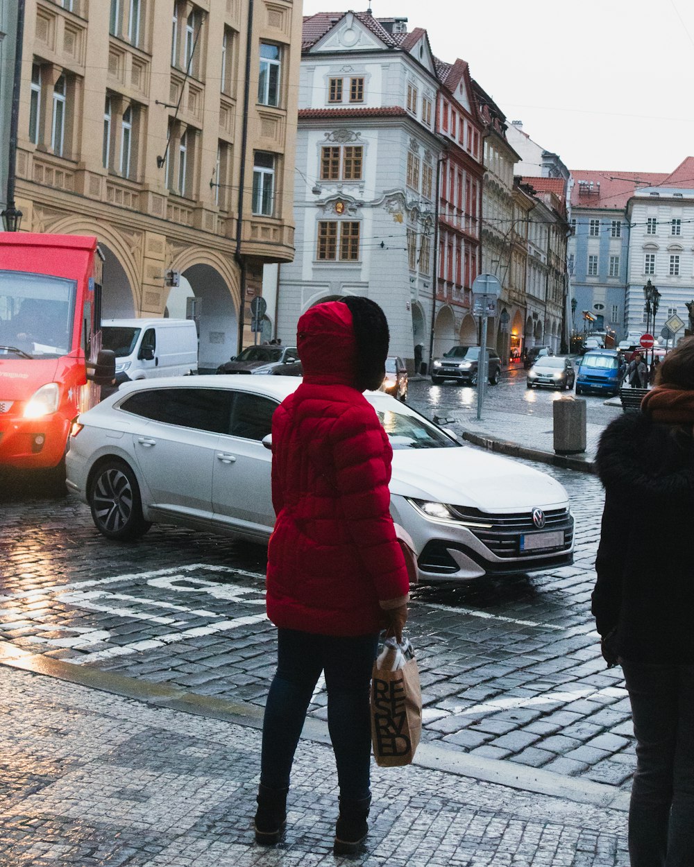 a woman in a red jacket is standing on a cobblestone street