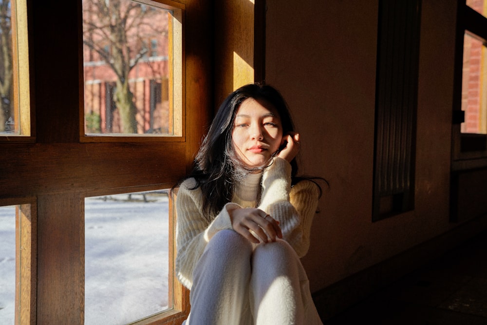 a woman sitting on a window sill with her hand on her head