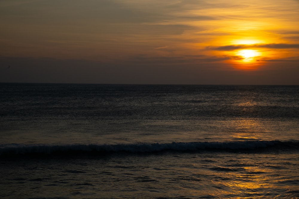 the sun is setting over the ocean on a cloudy day