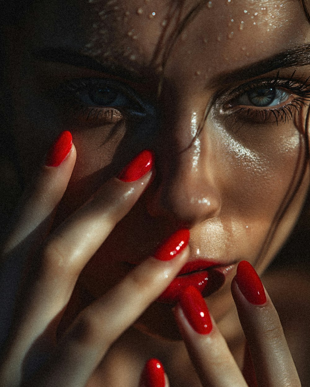 a woman with red nail polish holding her hands to her face